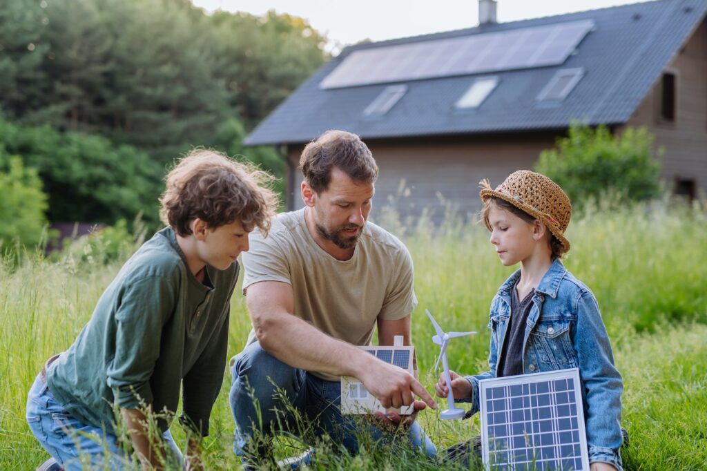 Father and his children holding solar panl standing in front of their house with photovoltaics on